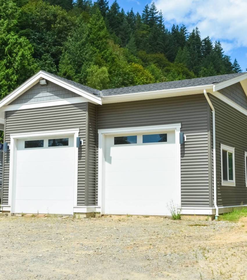 Brand new family house with car and boat parked on gravel driveway. New residential house and detached double garage on country side in British Columbia, Canada
